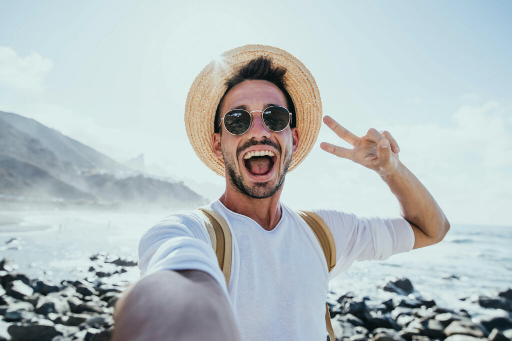 Happy man in sunglasses and a straw hat taking selfie on the beach