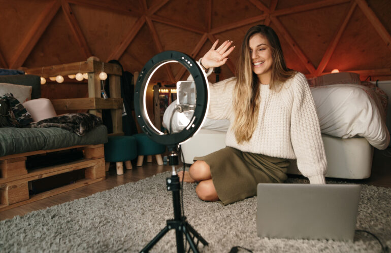 Woman influencer recording a video in her bedroom using her laptop, a smart phone and a light ring, inside a cozy wooden dome