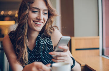 Smiling young woman holding phone and coffee cup in a coffee shop